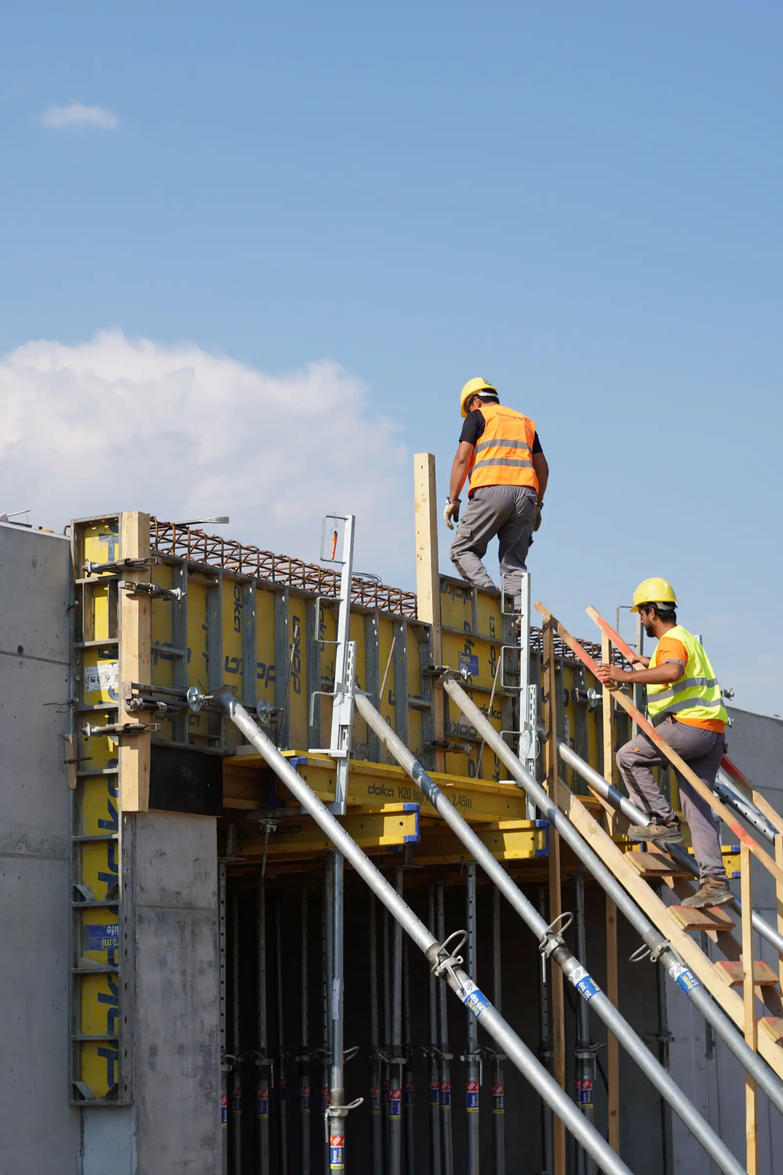 Zwei Bauarbeiter mit Schutzhelmen und Warnwesten bei Schalungsarbeiten auf einer Baustelle